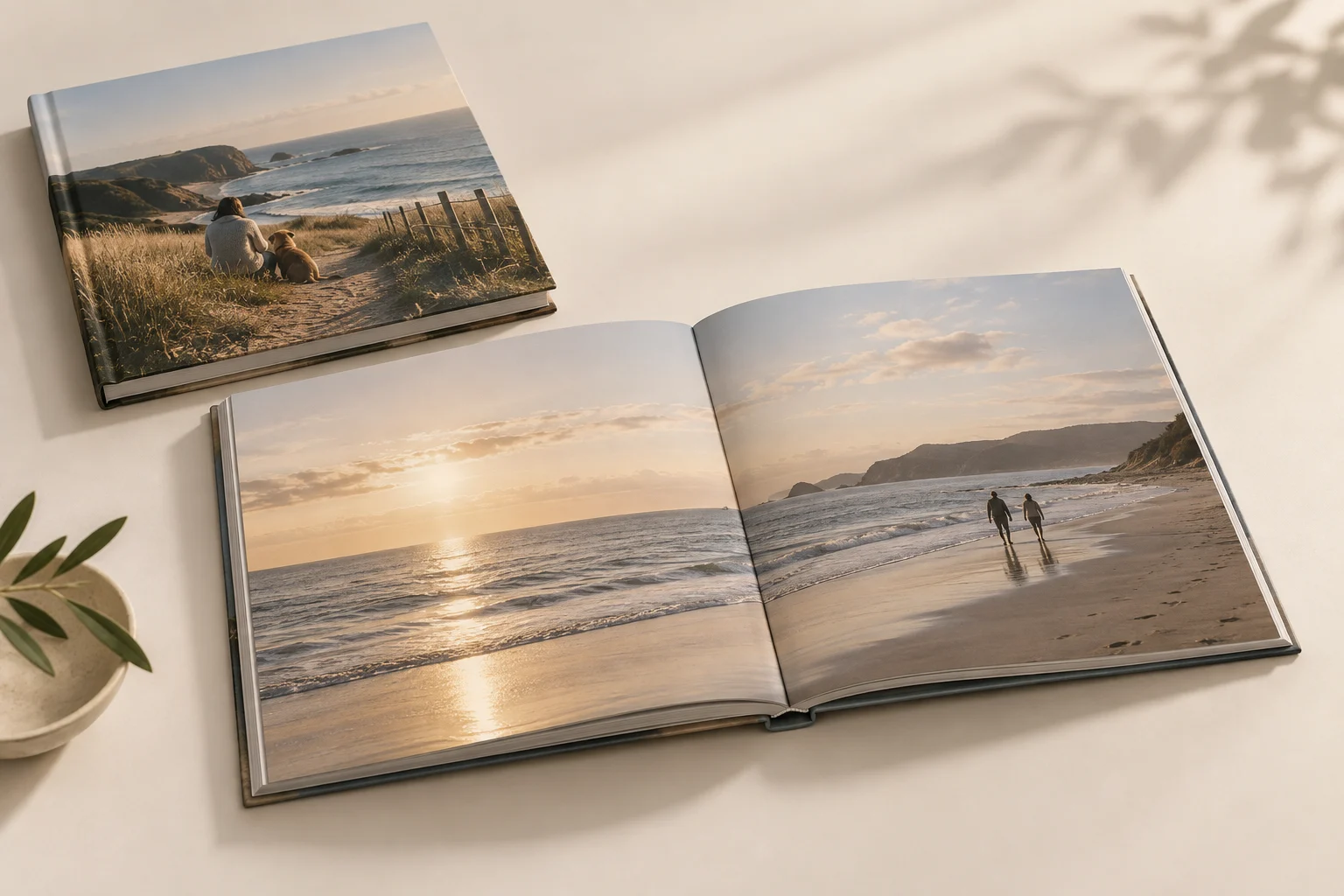 A closed hardcover photobook beside an open book with a coastal photo across two pages